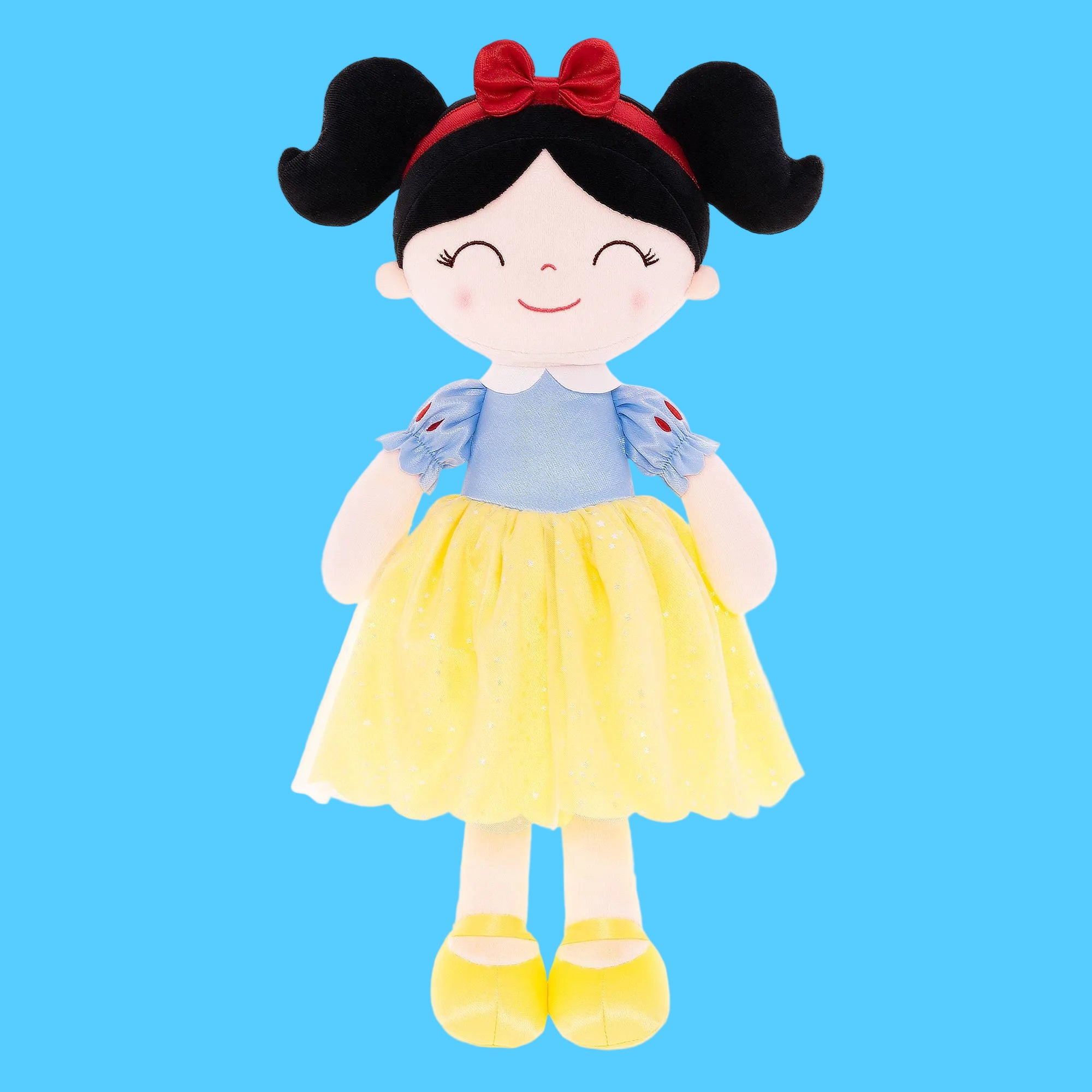 Boneca de pano artesanal da personagem Branca de Neve, com cabelo preto preso em duas chiquinhas, laço vermelho na cabeça, vestido com corpete azul brilhante e saia amarela rodada, sobre fundo azul claro.